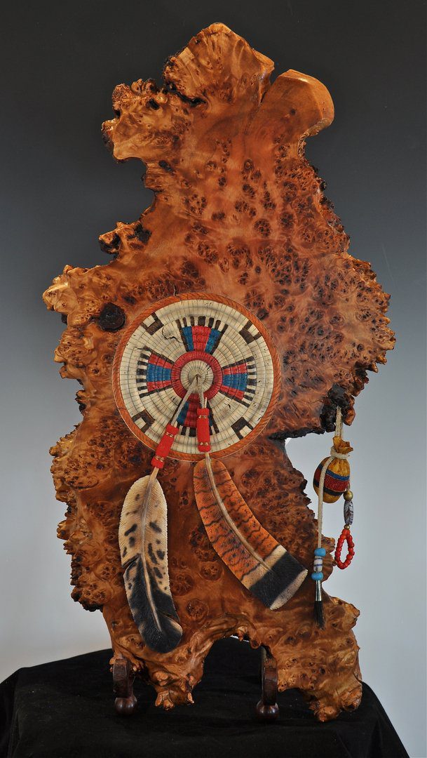 A wooden clock with feathers and beads hanging from it.