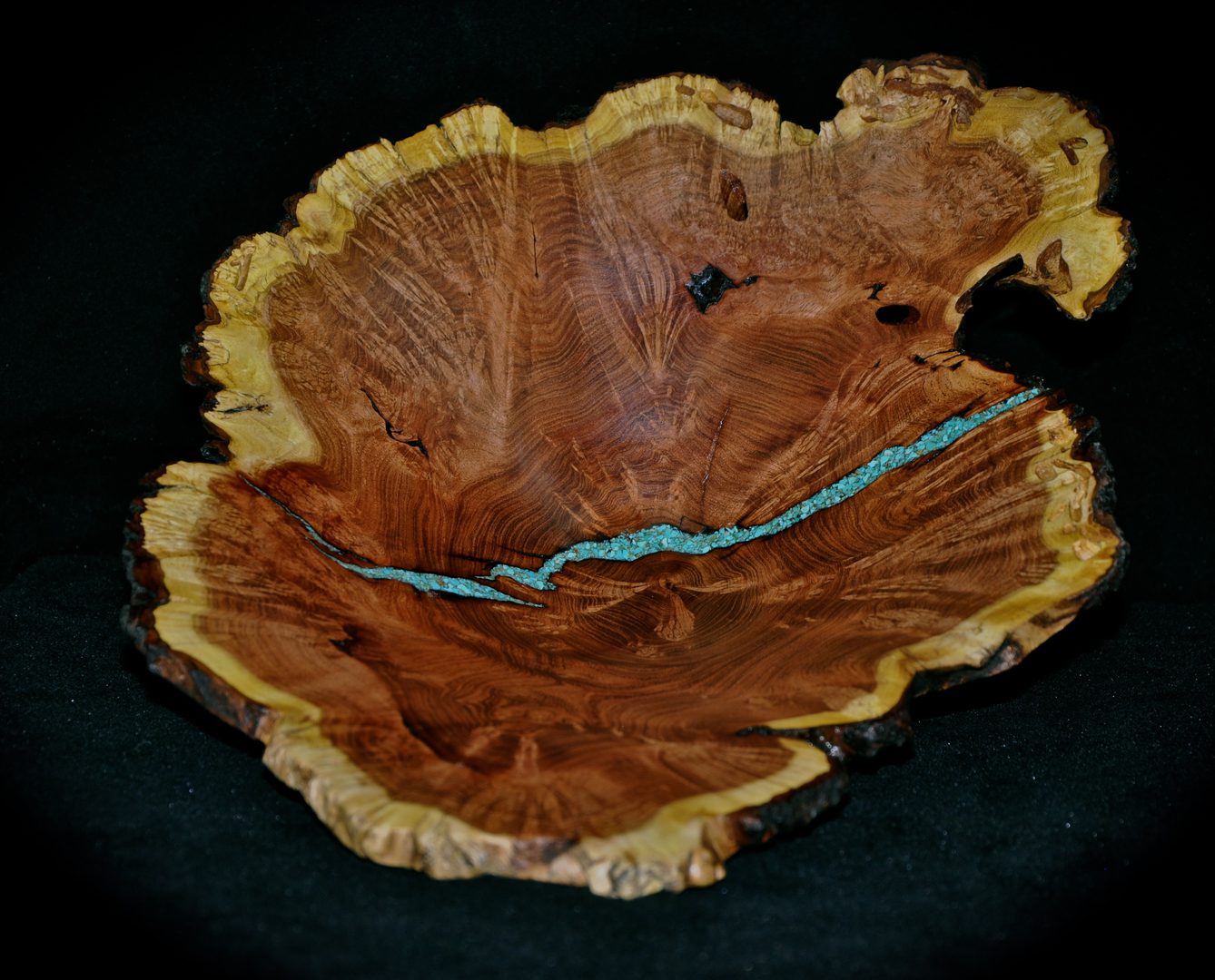 A wooden bowl with turquoise inlay on top of black background.